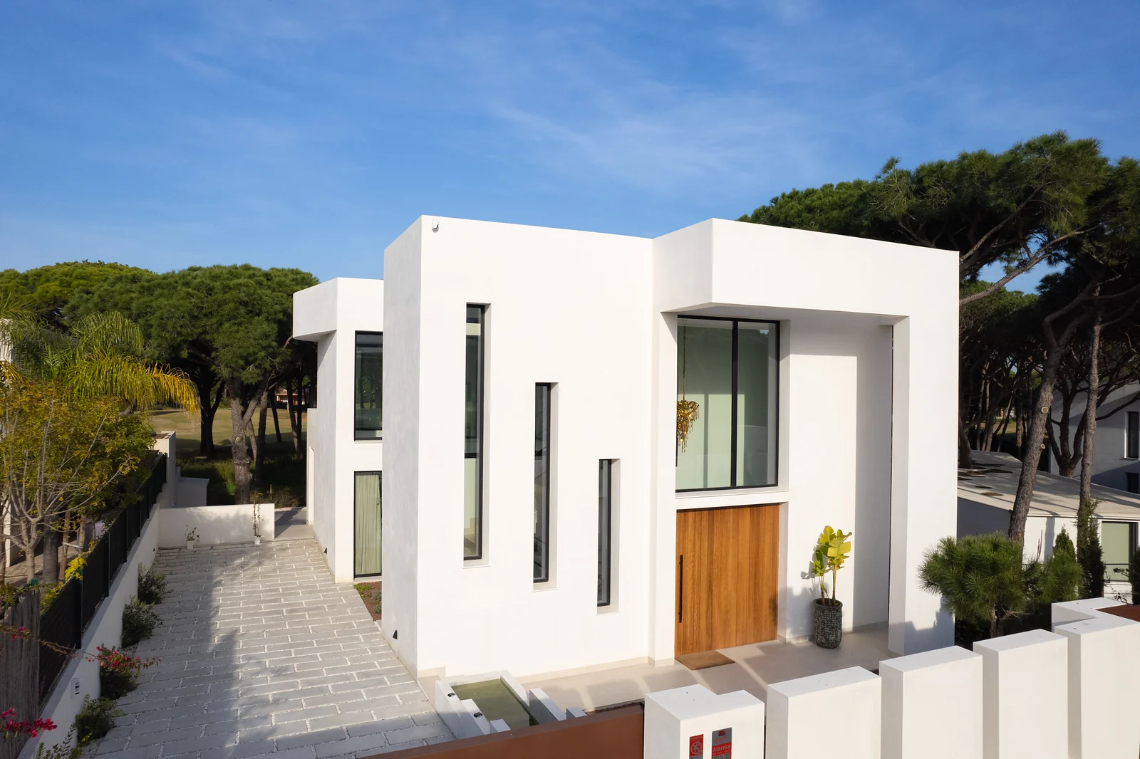 Villa Gatán: fachada de entrada con ventanas estrechas y puerta de madera bajo los pinos