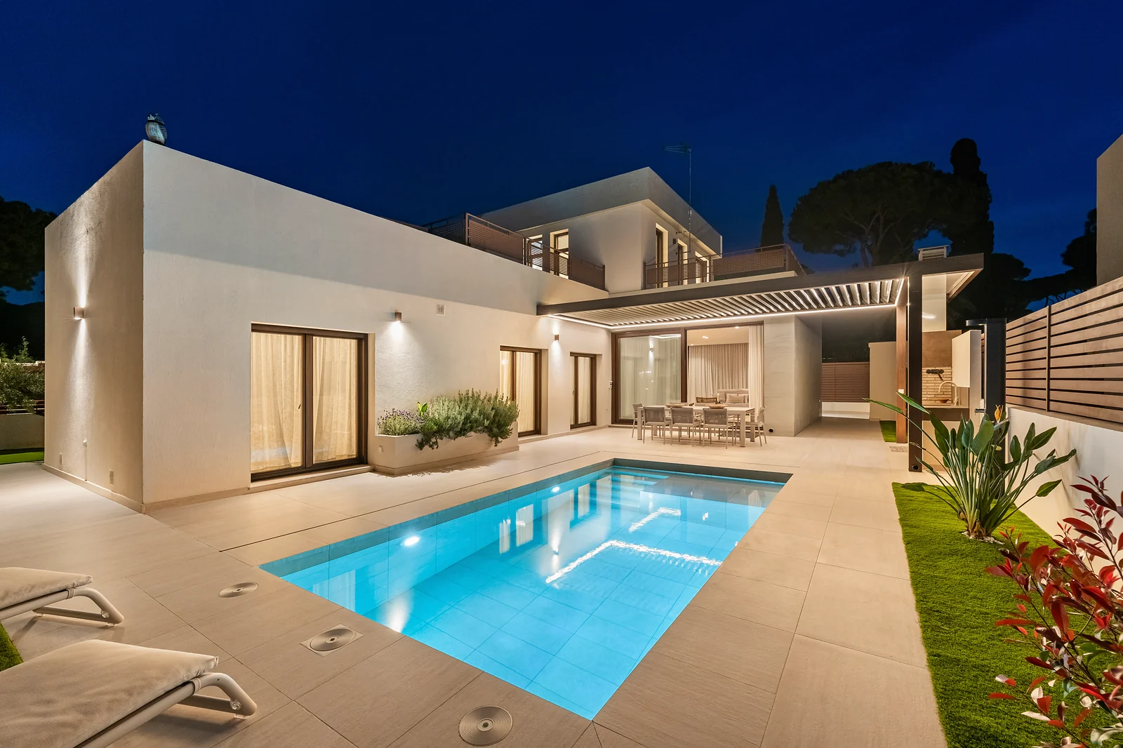 Villa Poniente a la hora azul: piscina iluminada frente a la villa blanca con pérgola