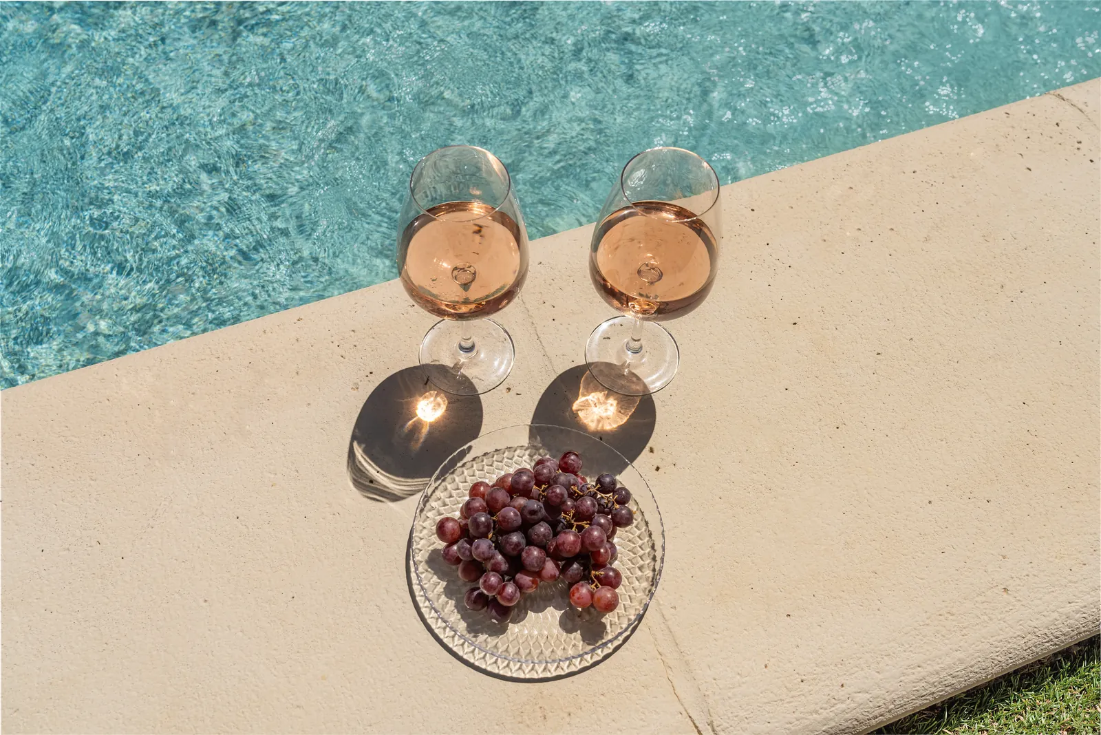 Two glasses of rosé and grapes at the pool edge