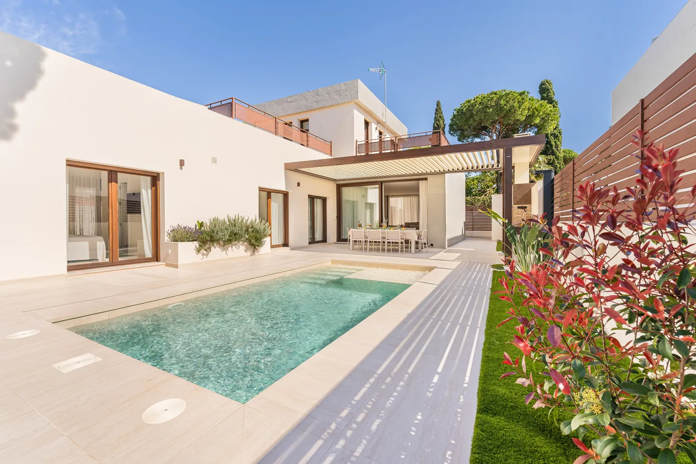 Villa Poniente de día: piscina frente a la casa blanca con pérgola y pinos