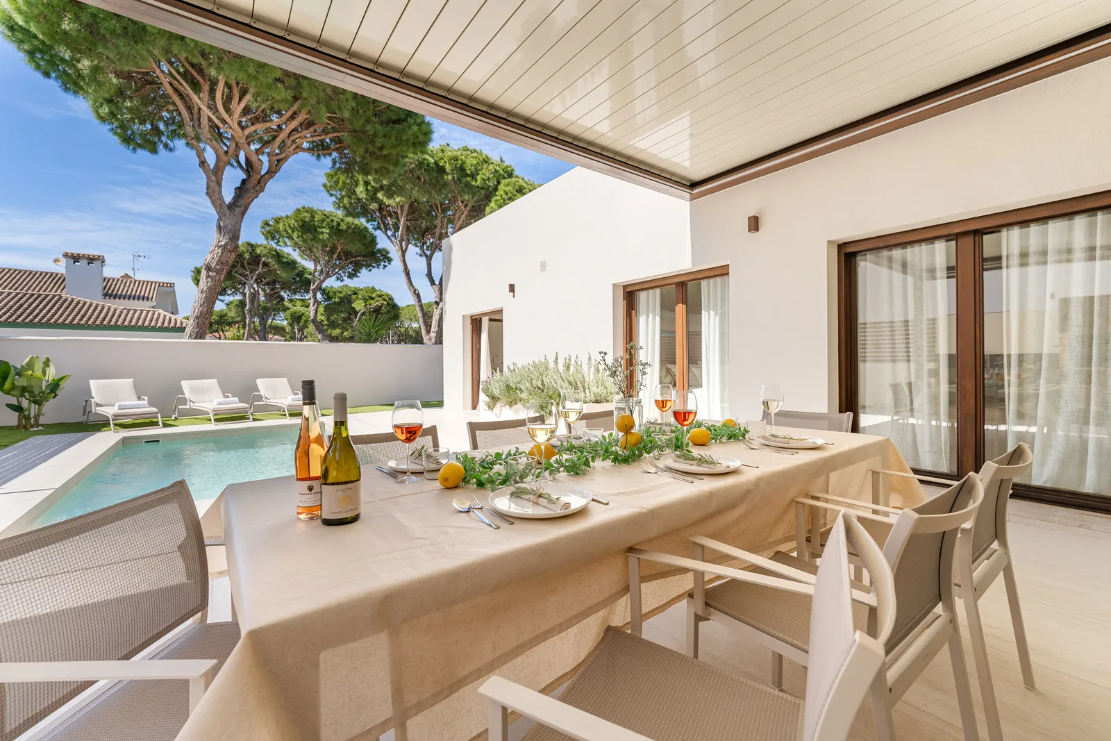 Table set under the pergola of Villa Poniente, with pool and pine trees behind